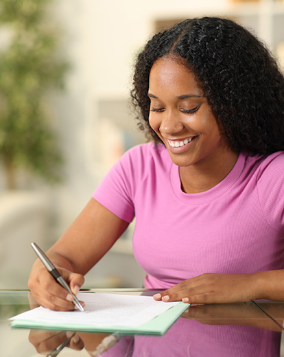 Junge Frau schreibt lächelnd auf ein Blatt Papier