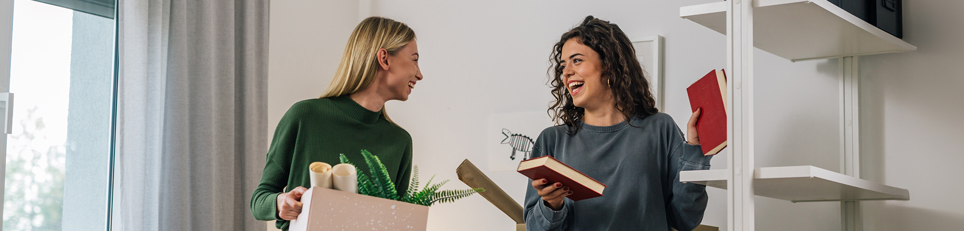 Zwei junge Frauen, die einen Karton und ein Buch halten