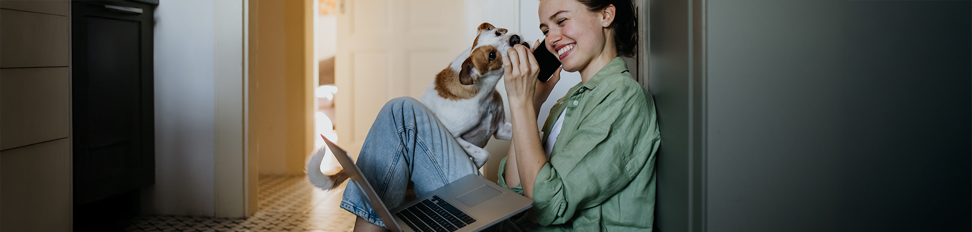 Junge Frau mit Laptop auf dem Boden sitzend wird von Hund abgeleckt