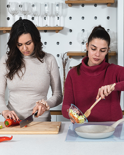 Zwei junge Frauen kochen gemeinsam und schneiden Gemüse