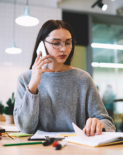Junge Frau sitzt an einem Tisch und hat ihr Handy am Ohr