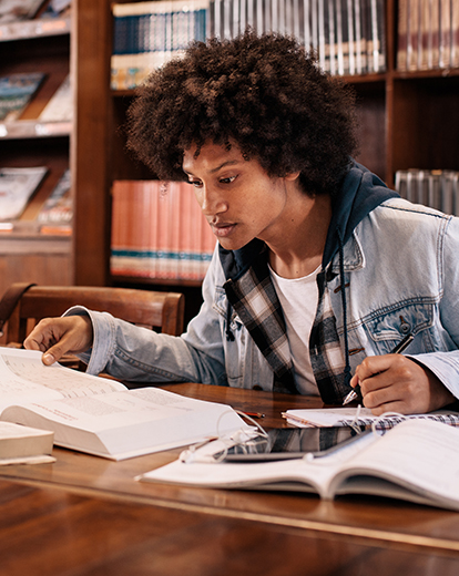 Junger Mann in einer Bibliothek über Bücher gebeugt