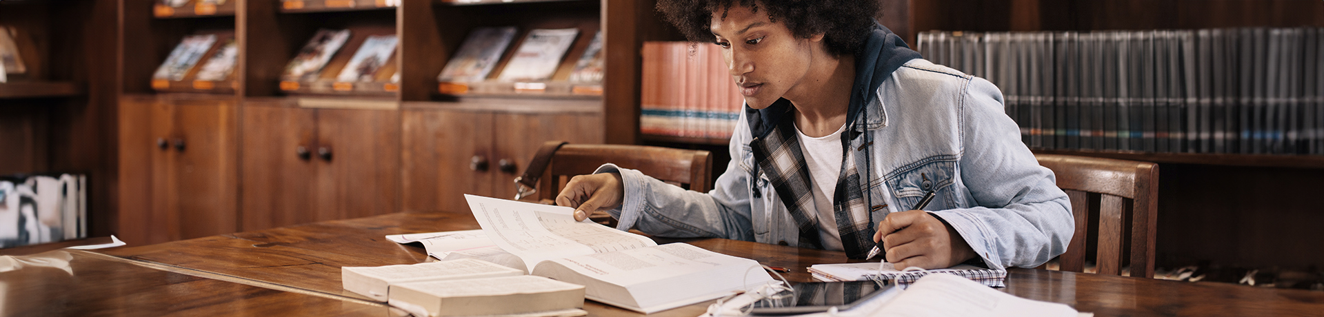 Junger Mann in einer Bibliothek über Bücher gebeugt