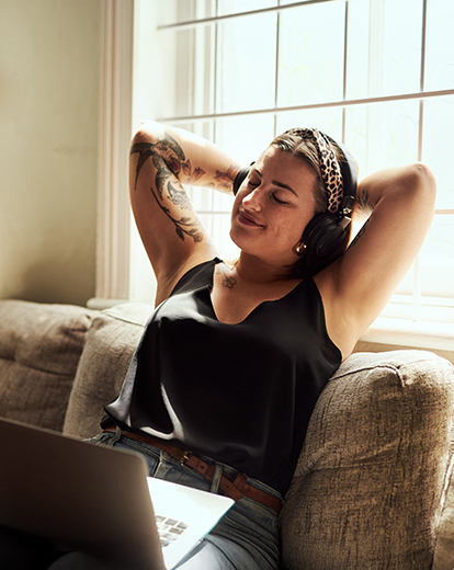 Junge Frau entspannt mit Kopfhörern zurückgelehnt auf einer Couch