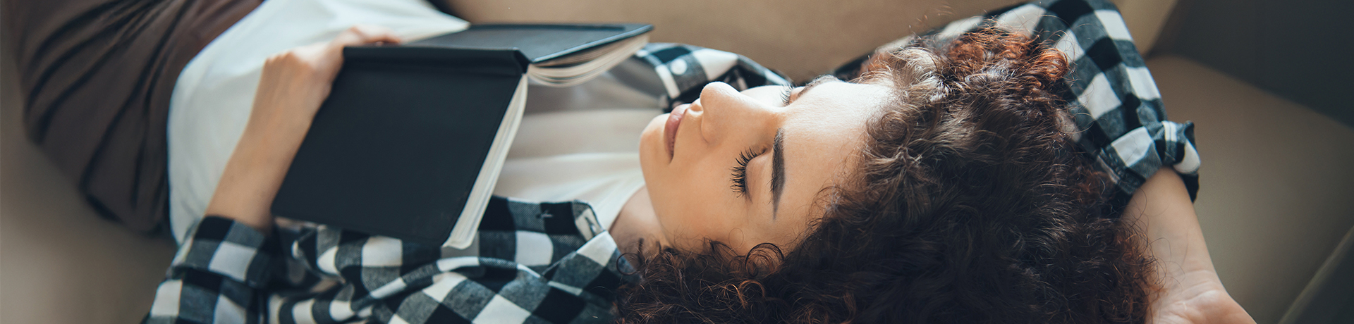 Junge Frau ist mit Buch auf der Brust auf dem Sofa eingeschlafen