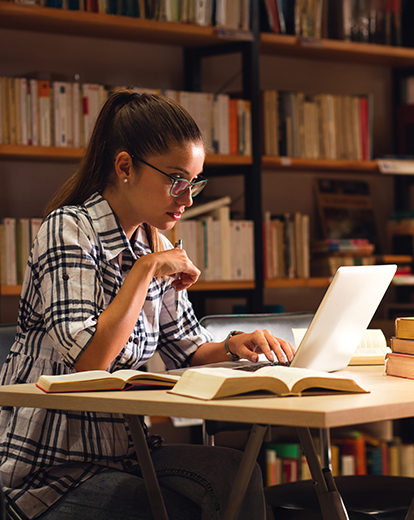 Studentin in einer Bibliothek vor ihrem Laptop
