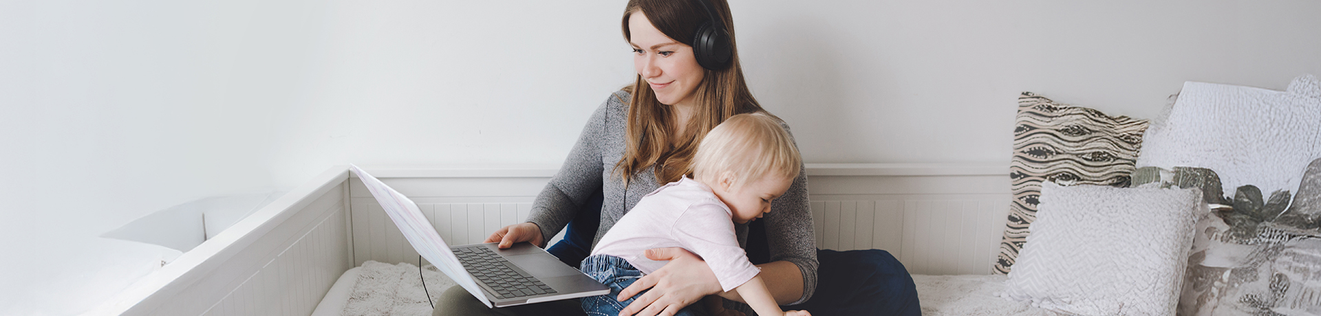 Junge Frau mit Kind auf dem Schoß blickt in einen geöffneten Laptop