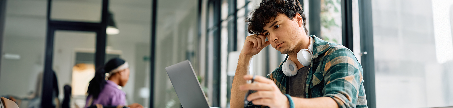Junger Mann schaut nachdenklich in einen Laptop, den Kopf auf eine Hand gestützt